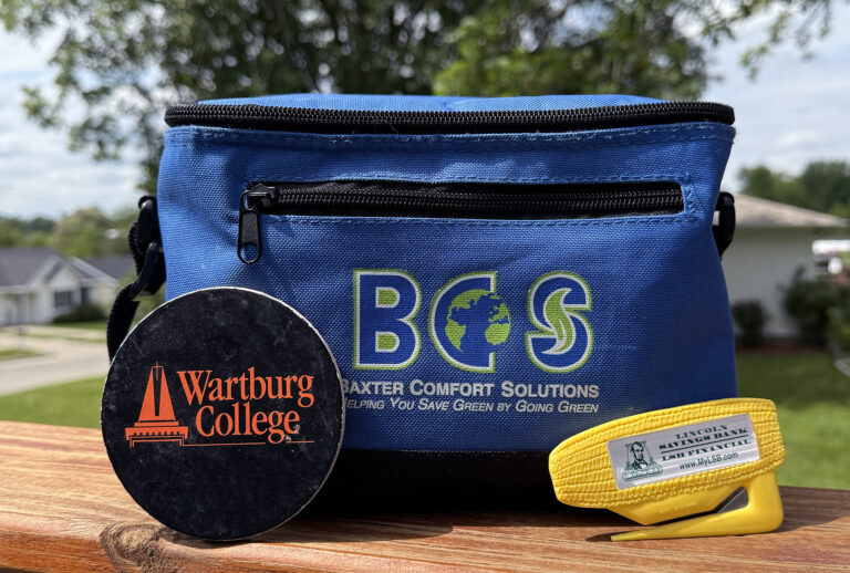 A photo featuring a black logoed coaster, a blue lunch cooler bag and a yellow letter opener.