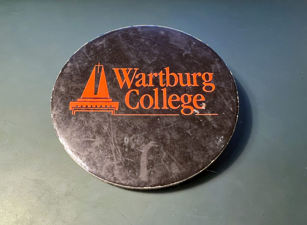 Photo of a black coaster with an orange logo from Wartburg College.