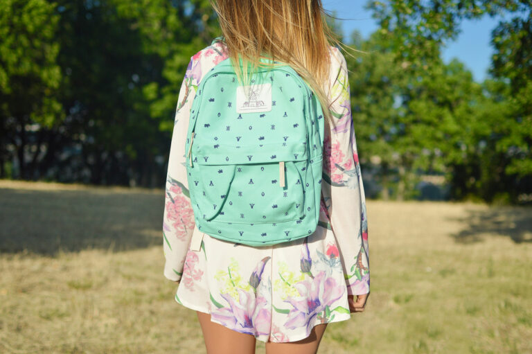 Girl wearing a green branded backpack standing in an open green space.