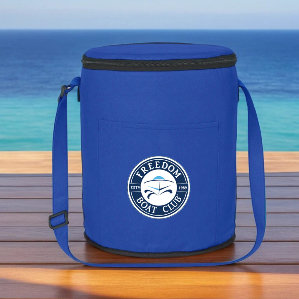 Blue Freedom Boat Club cooler bag on a wooden surface with ocean in the background.