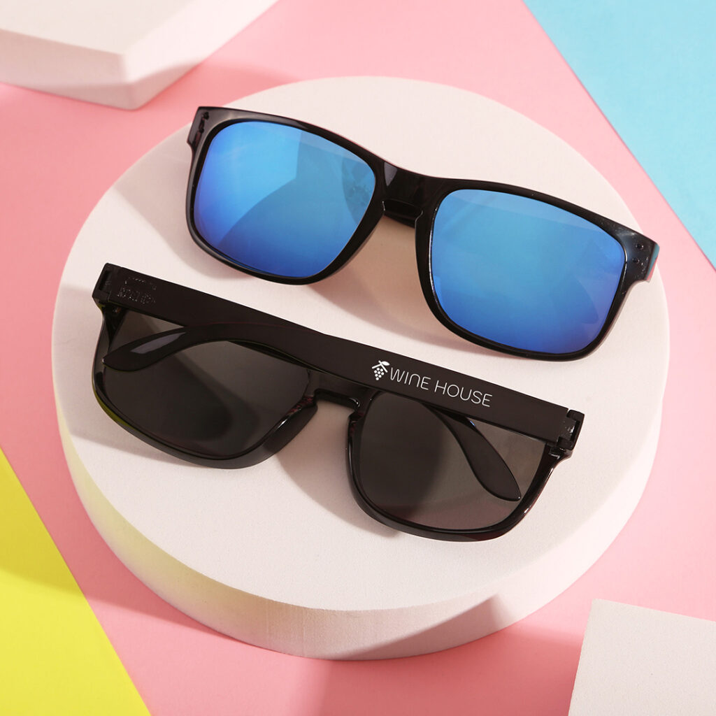 Two black-framed sunglasses on a white platform with a pastel geometric background.