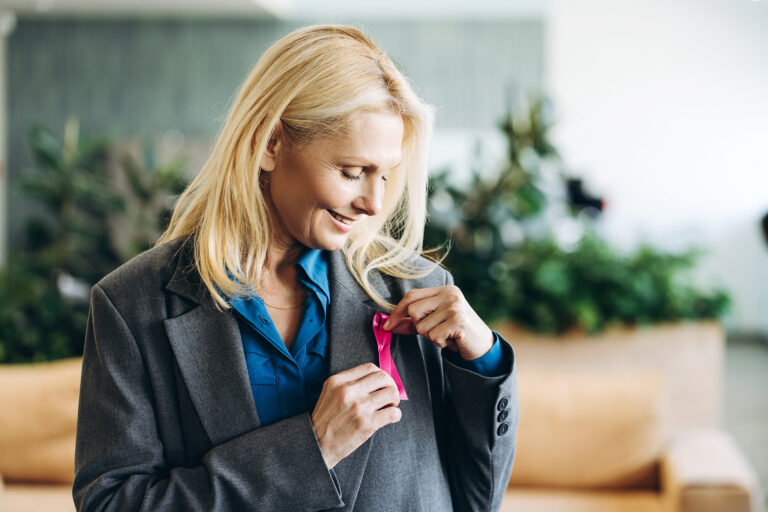 Person pinning a pink ribbon to their blazer.