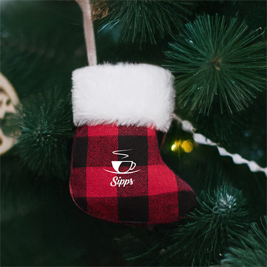 Red and black plaid Christmas stocking with white faux fur trim hanging on a decorated green tree.