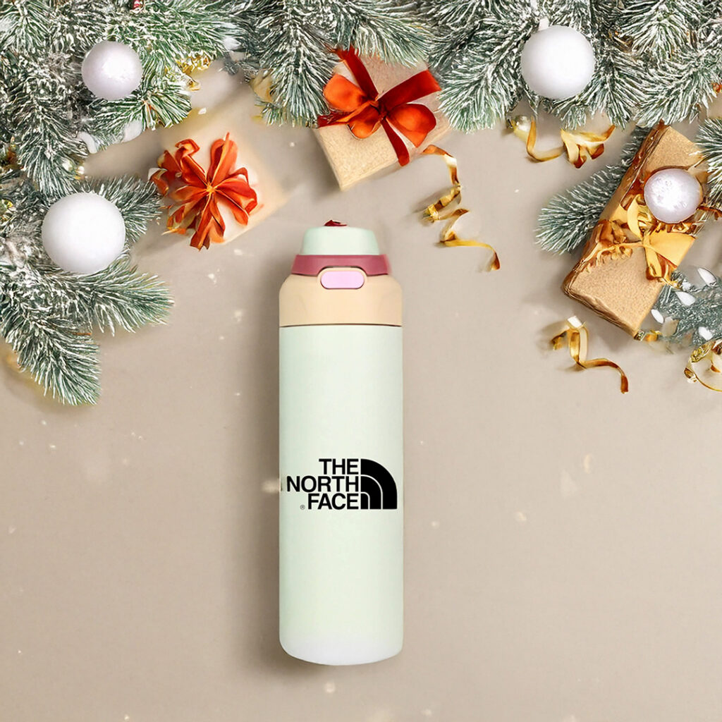 North Face water bottle placed on a festive holiday background with pine branches, ornaments, wrapped gifts and golden ribbons.
