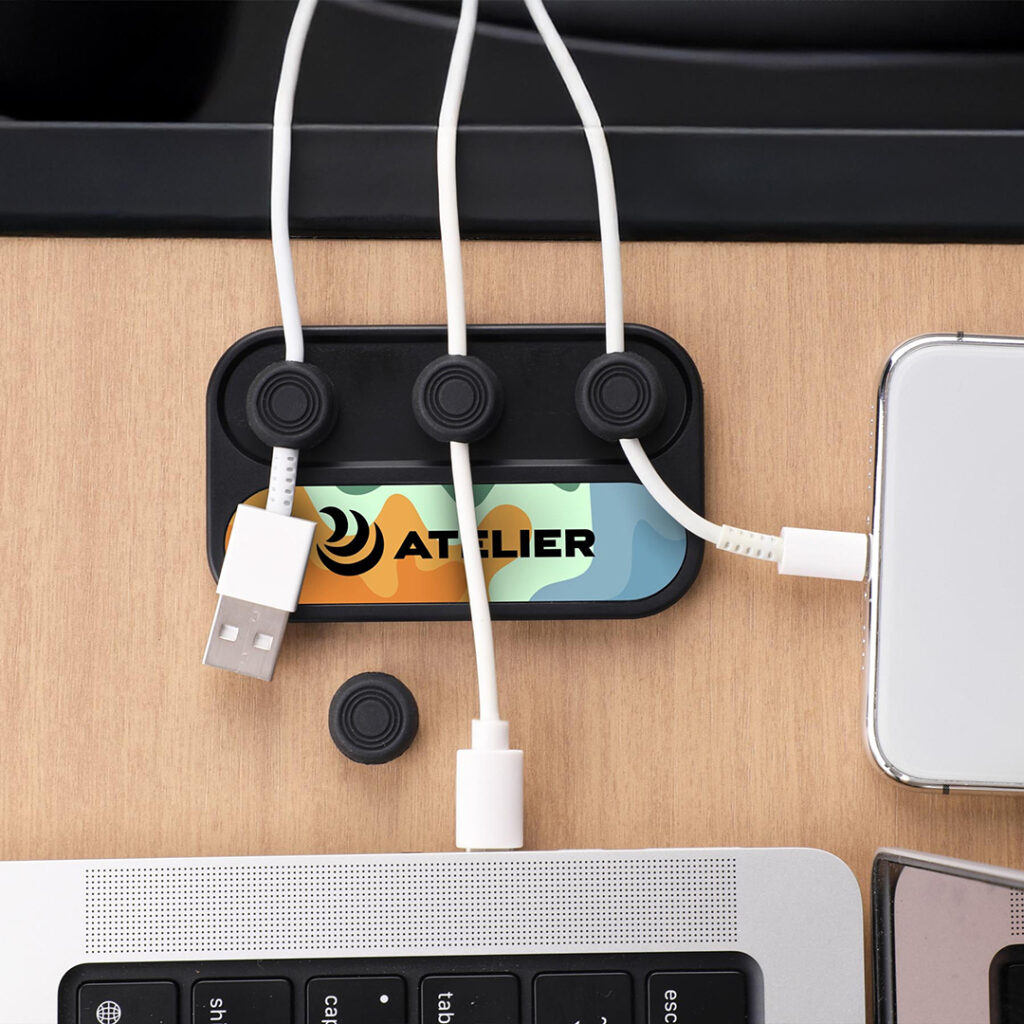 Cable organizer holding three white charging cables on a wooden desk next to a laptop keyboard and smartphone.
