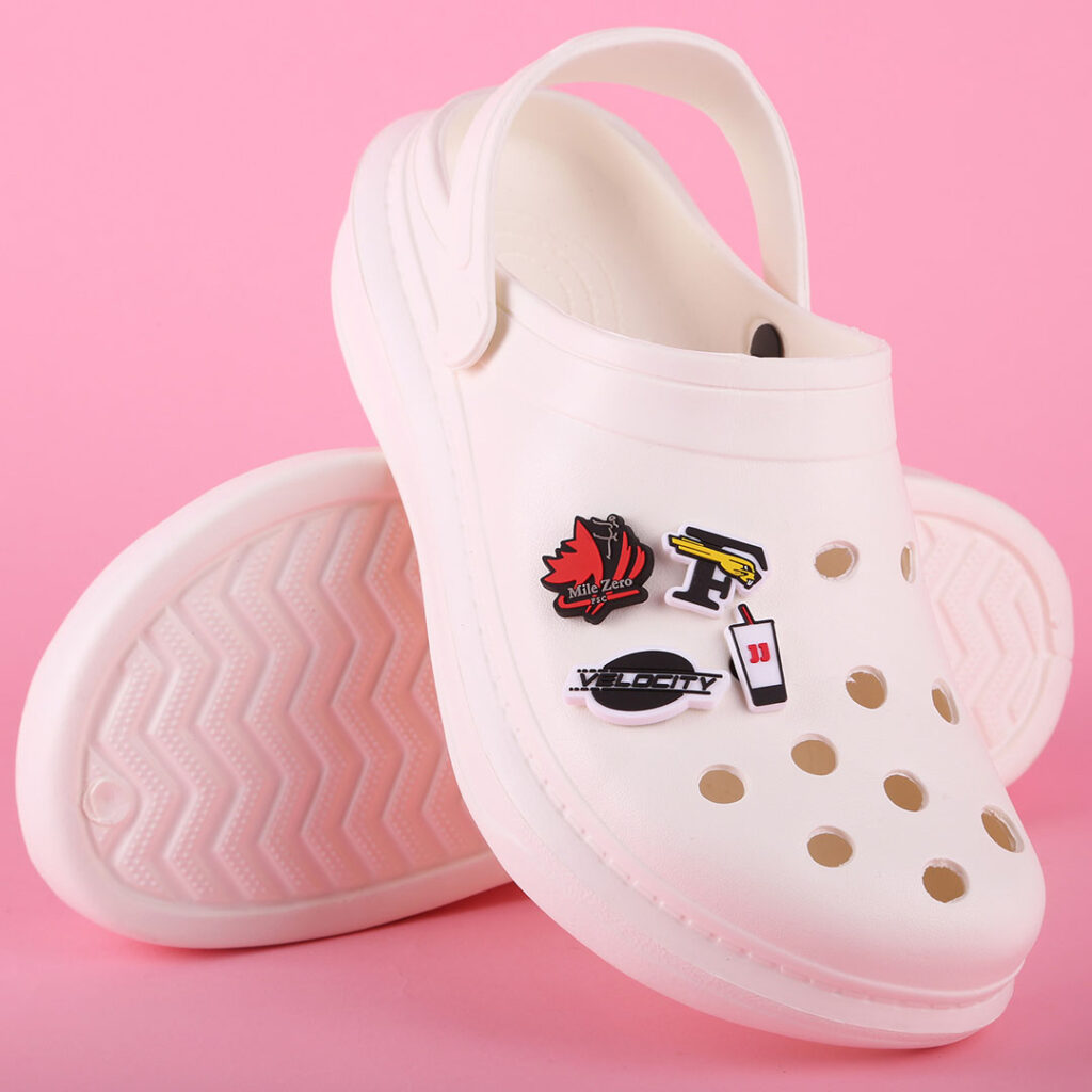 White clogs with custom shoe charms on a pink background.