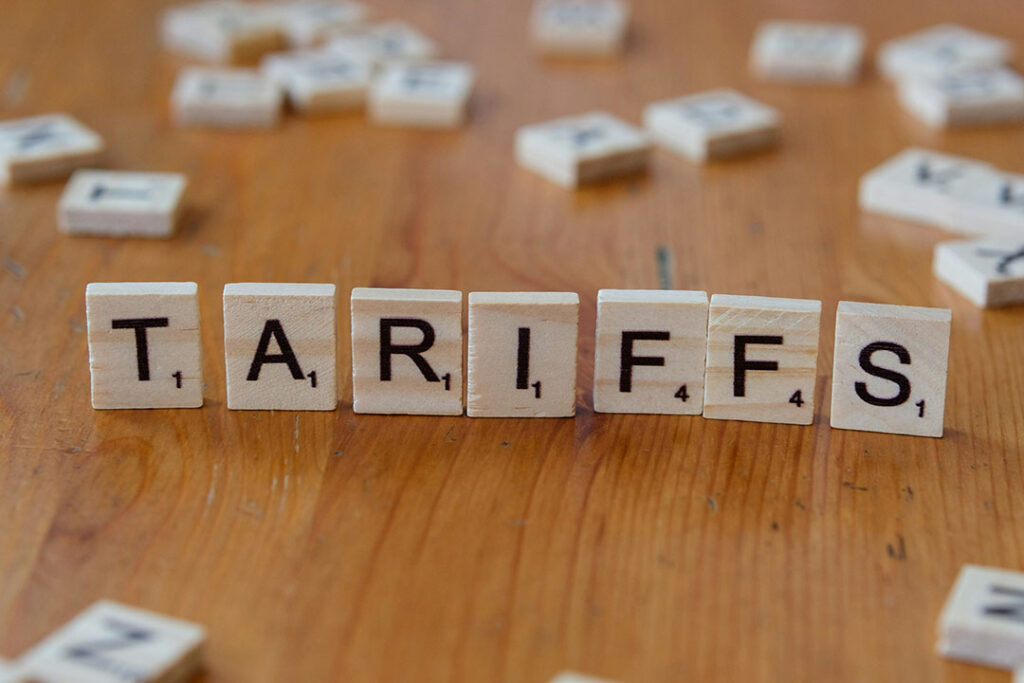 Scrabble tiles spelling the word “TARIFFS” on a wooden surface with scattered tiles in the background.