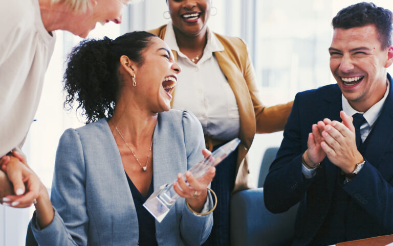 Employees celebrating a workplace achievement as a team member holds an award during an office recognition event.