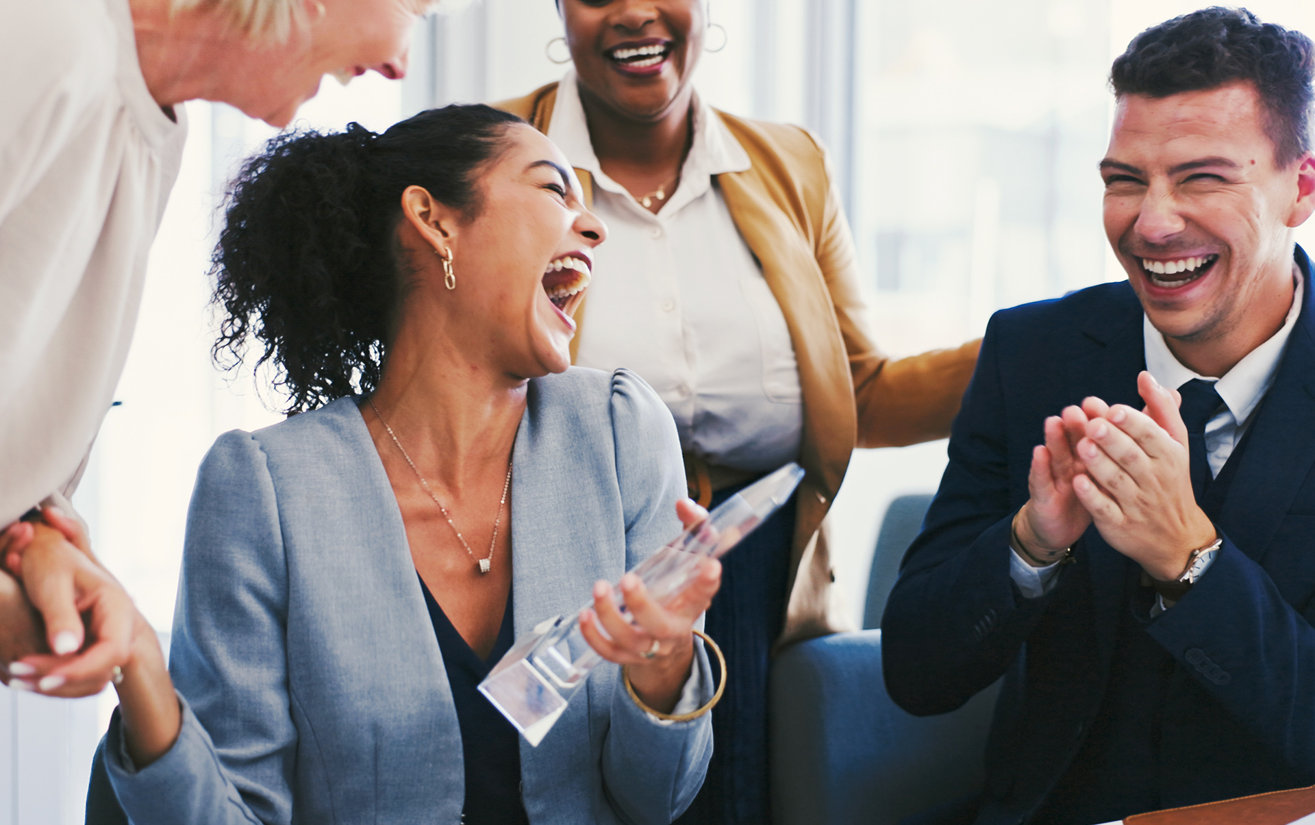 Employees celebrating a workplace achievement as a team member holds an award during an office recognition event.