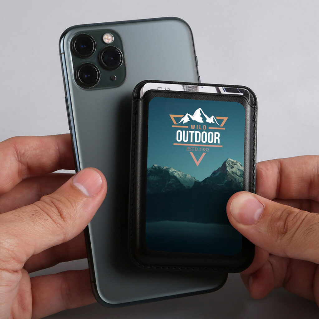 Hands holding a smartphone with a branded magnetic wallet attached, featuring an outdoor mountain design and the text ‘Wild Outdoor ESTD. 1983.’