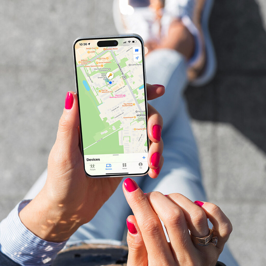 Close‑up of hands holding a smartphone displaying a map app while sitting outdoors on a paved surface.