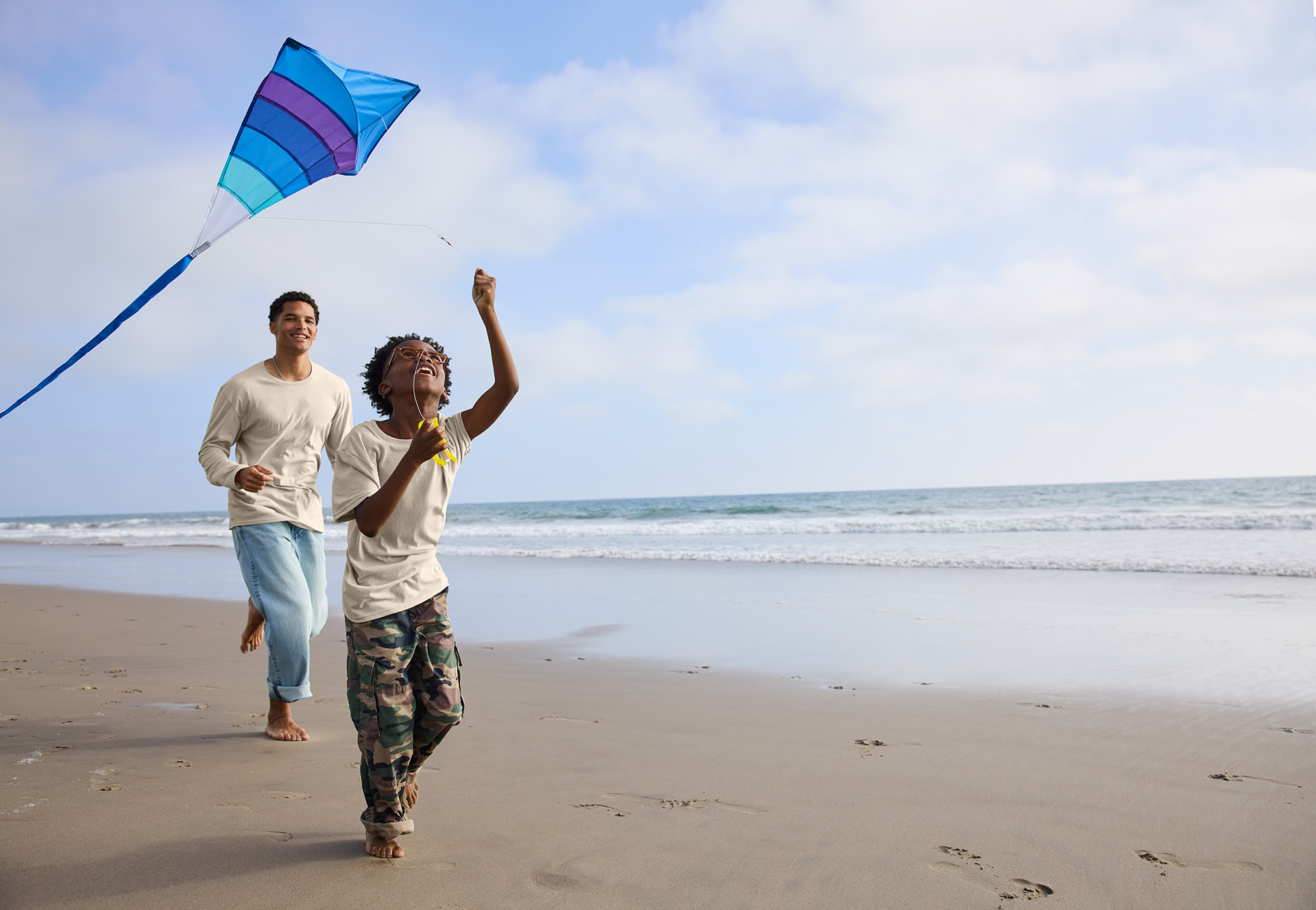 Two people flying a colorful kite on a beach with ocean waves and blue sky in the background.
