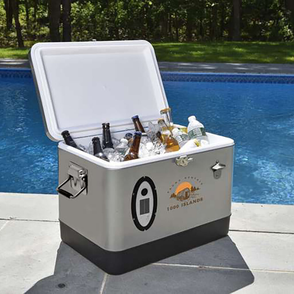 Open cooler filled with ice and assorted bottled drinks sitting poolside on a sunny day, with a built-in bottle opener on the side.