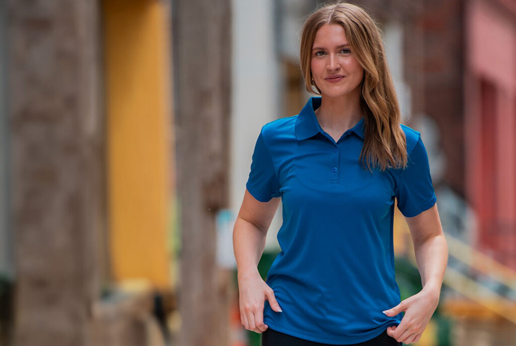 Person wearing a blue short-sleeve polo shirt standing outdoors in an urban setting.