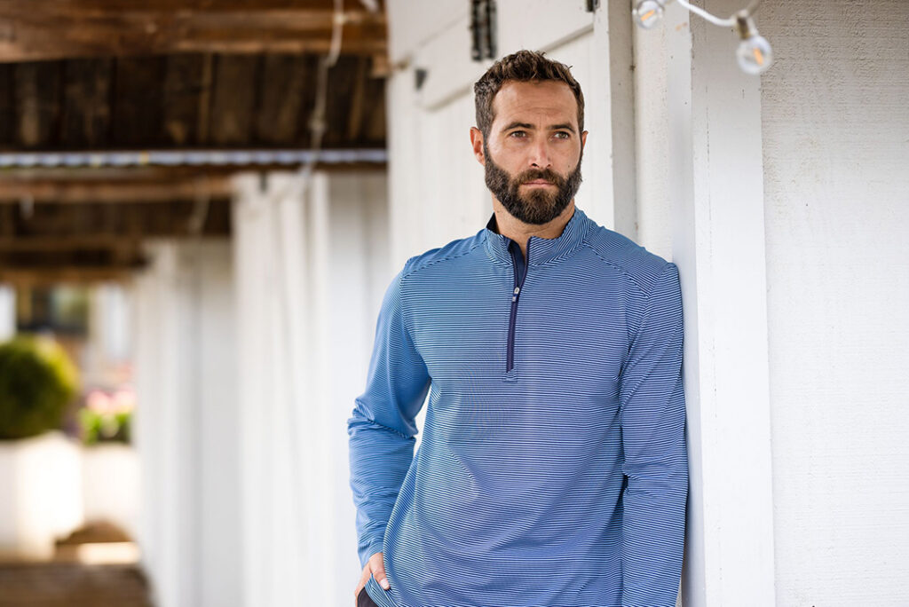 Person wearing a blue striped quarter-zip top leaning against a white wall outdoors.