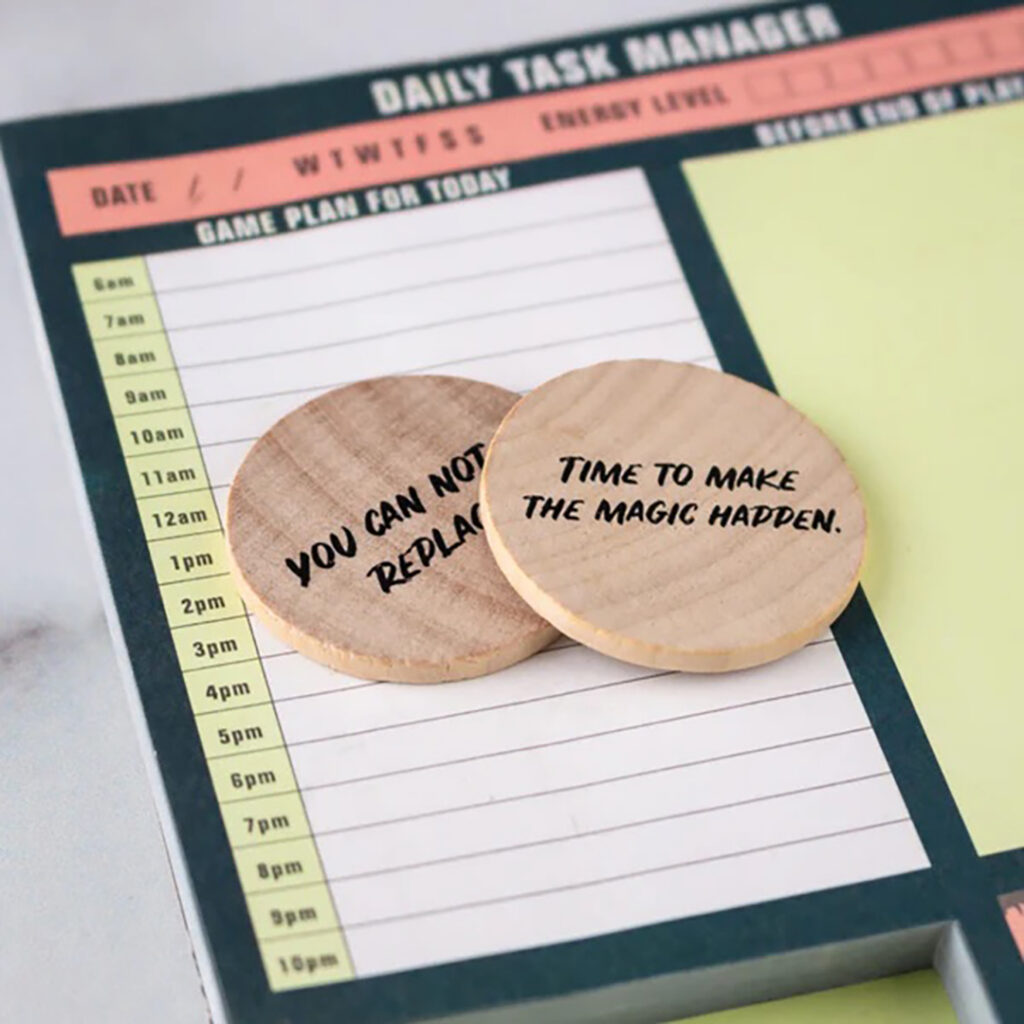 “Daily Task Manager” planner page with two round wooden tokens on top, each printed with motivational phrases.