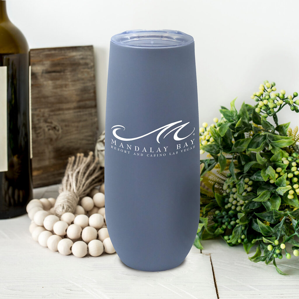 Matte blue insulated tumbler with white “Mandalay Bay Resort and Casino Las Vegas” logo displayed on a styled tabletop with neutral decor, representing elevated, understated branded drinkware.