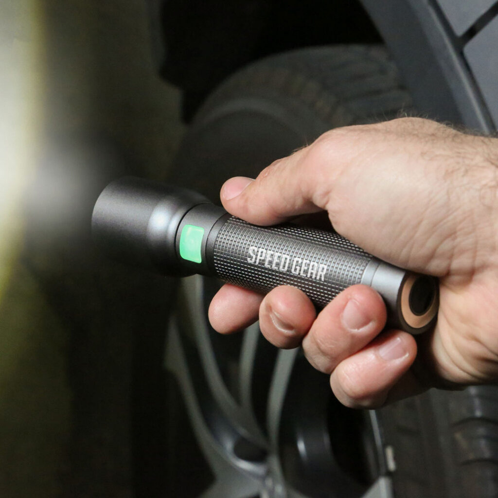Custom-branded LED flashlight being used near a vehicle tire, showcasing a promotional tool with printed company branding and illuminated power button.