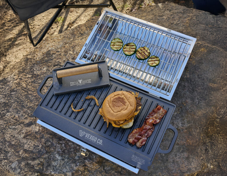 Branded tailgating grill set featuring a custom grill press, burger, bacon and grilled zucchini on an outdoor portable grill.