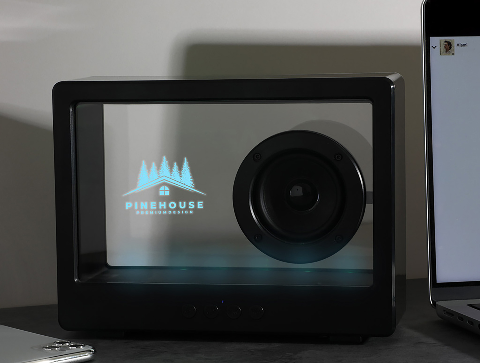 Branded wireless speaker with a clear display projecting a company logo on a desktop workspace.