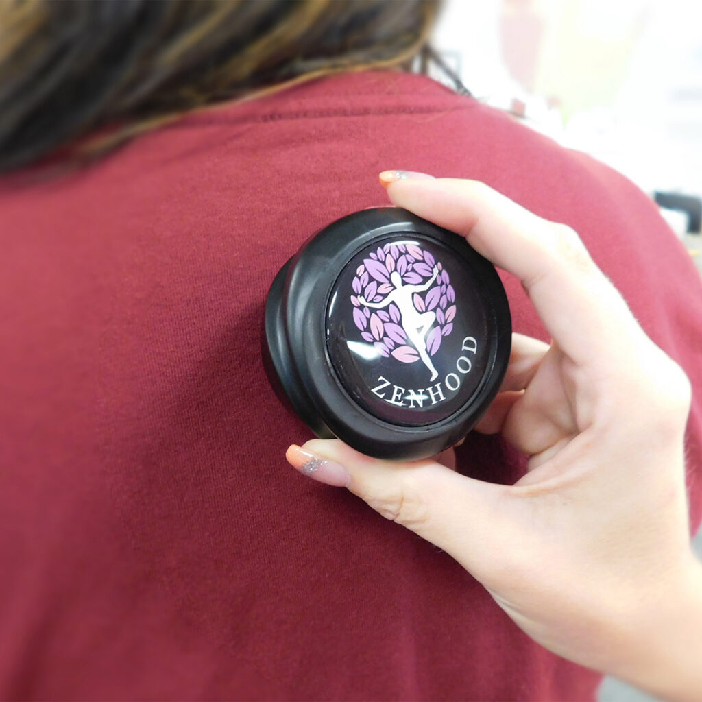Hand holding a massage therapy tool against a person's upper back to help relieve muscle tension and stress.