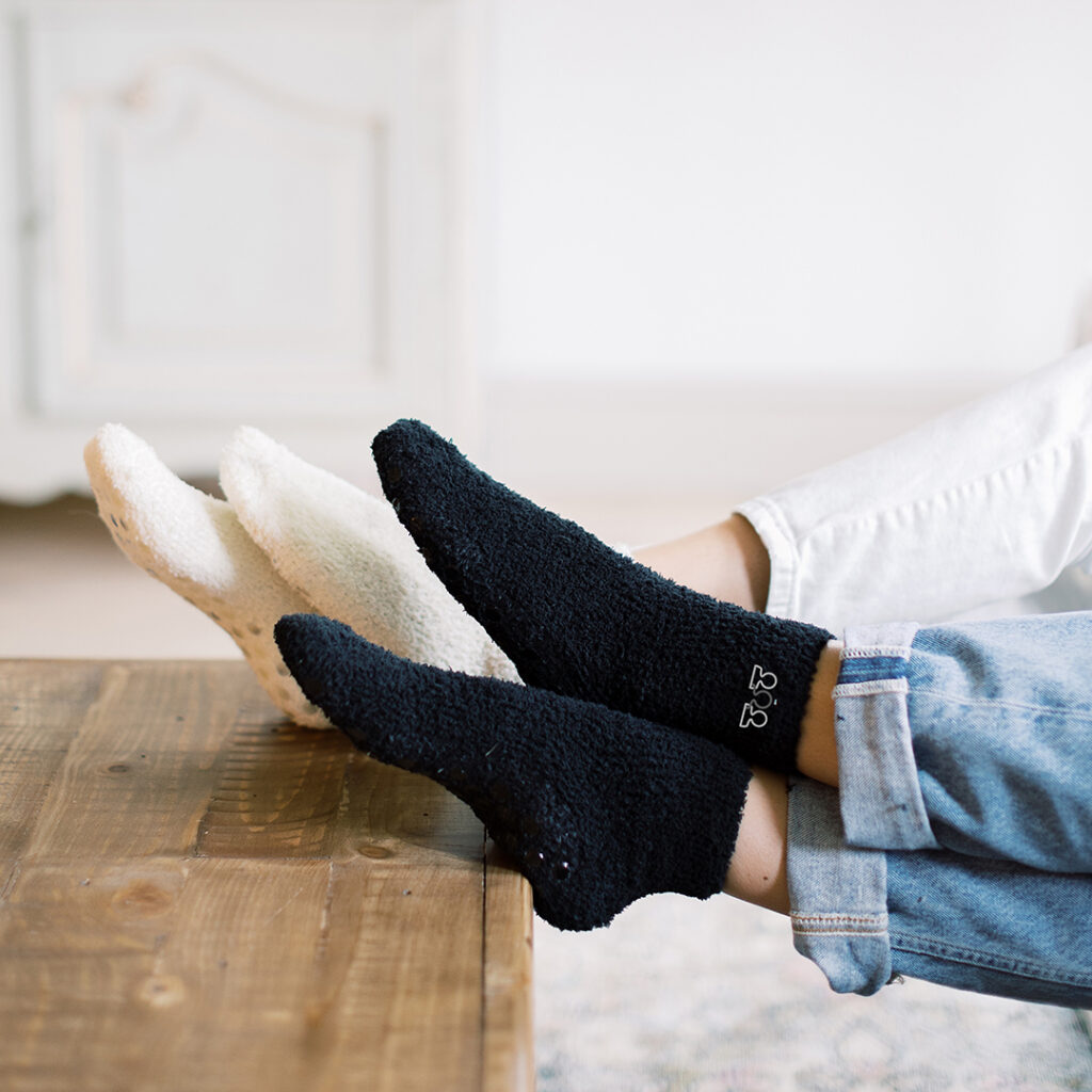 Person resting with feet up on a wooden table, wearing cozy socks and rolled-cuff jeans in a relaxing home setting.