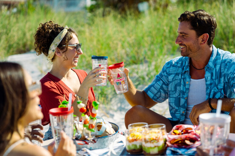 Tourism gift shop souvenir cups and tumblers being used by visitors at a beach gathering, highlighting memorable travel keepsakes.