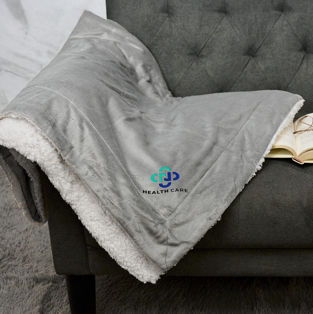 Soft fleece blanket with embroidered company logo draped over a chair, representing a cozy and memorable holiday gift for clients and employees.