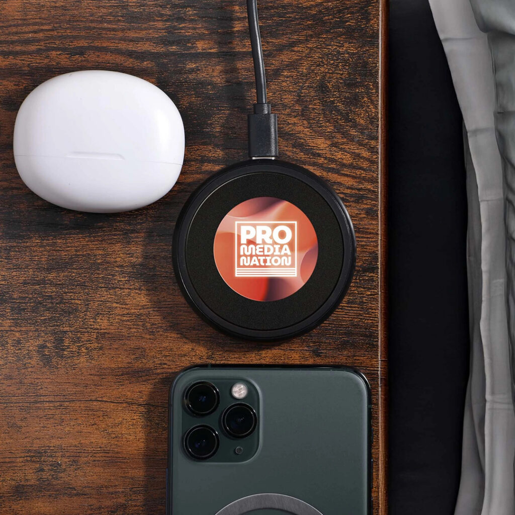 Custom wireless charging pad and earbuds displayed alongside a smartphone, highlighting popular branded tech gifts for holiday giving.