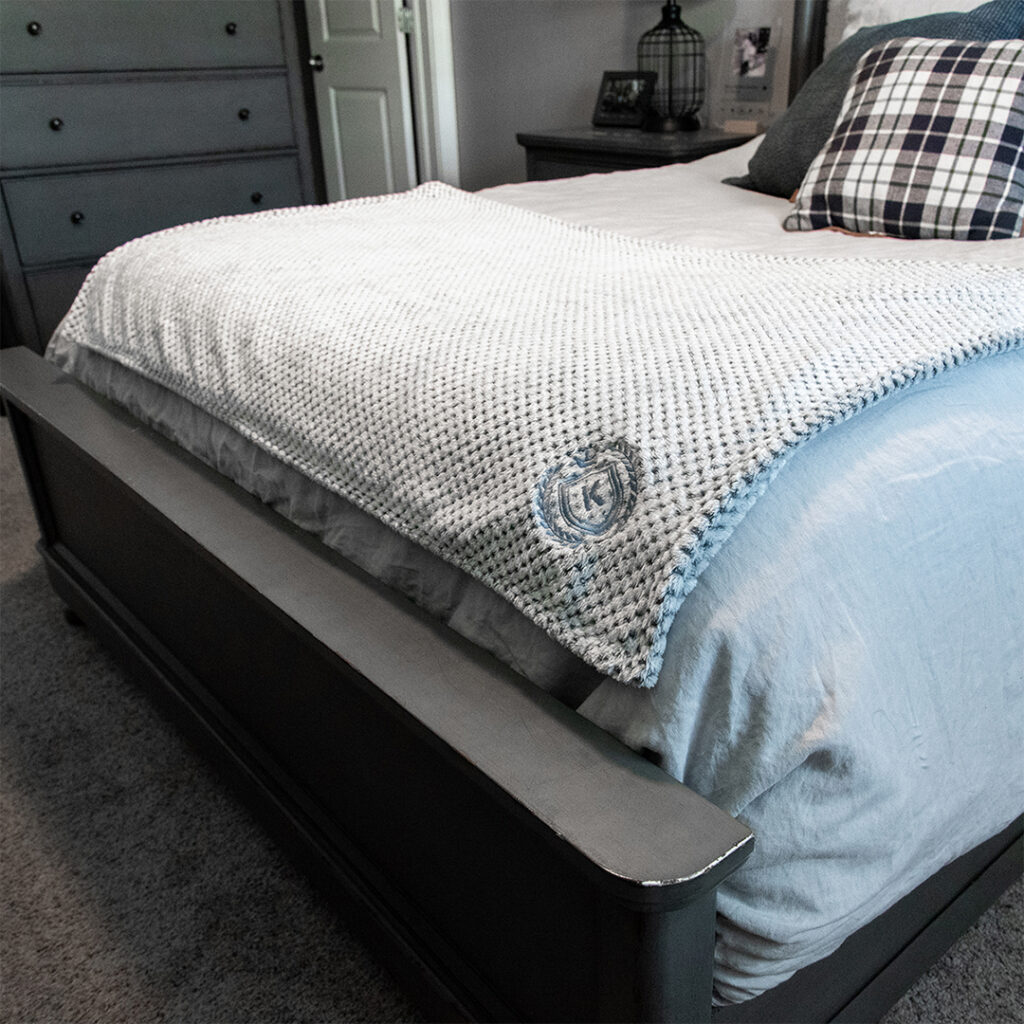 Premium embroidered blanket draped over a bed, showcasing the comfort and upscale look of branded blankets for gifts, recognition programs and home use.