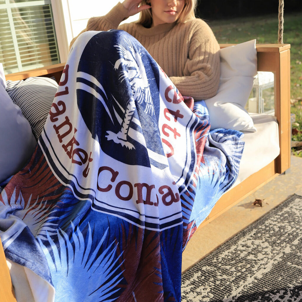 Custom printed fleece blanket with vibrant full-color branding displayed in an outdoor lounge setting, demonstrating a popular promotional blanket option.