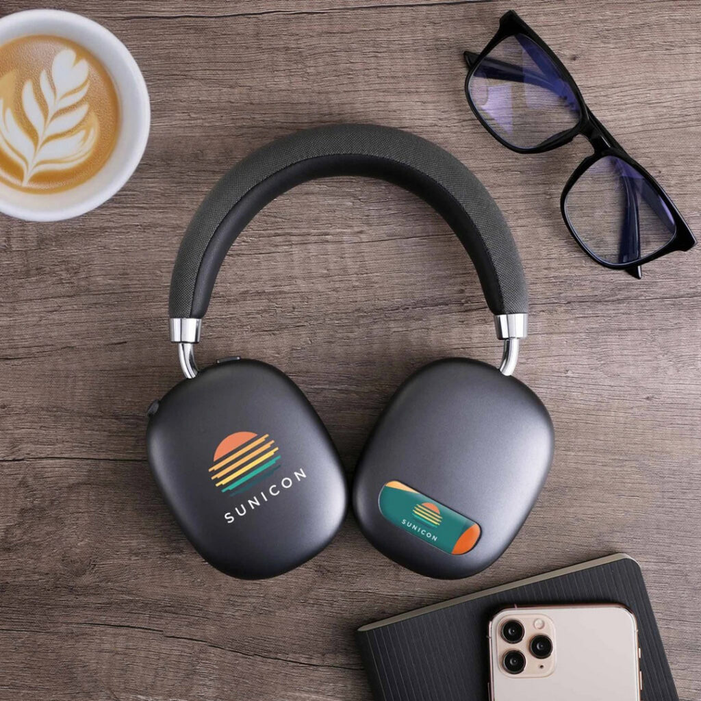 Wireless over-ear headphones displayed beside a smartphone, coffee and glasses, showcasing a tech-forward gift for someone who enjoys gadgets and everyday connectivity.